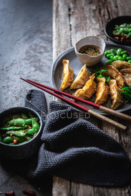 Gyozas with green beans and soy sauce with sesame seeds placed with chopsticks near bowls with spices and pea pods — Stock Photo