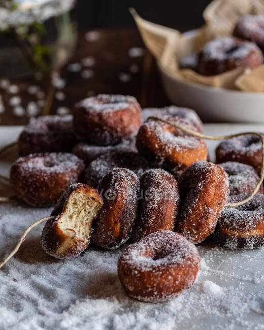 Аппетитные сладкие пончики на нитке на столе с разбросанным сахарным порошком — стоковое фото