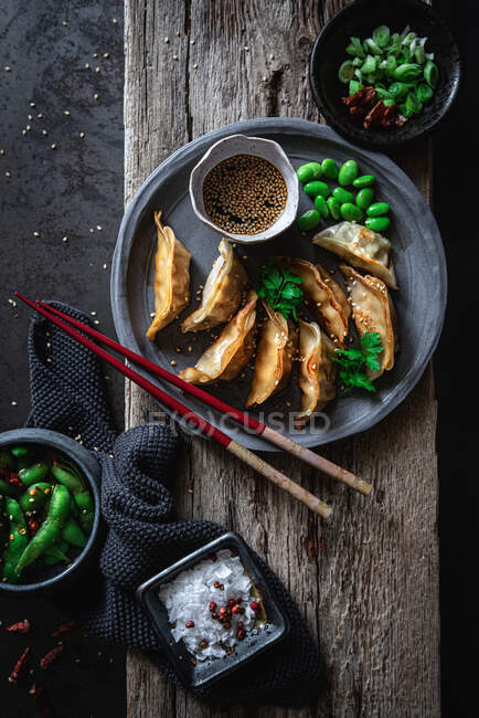 Gyozas mit grünen Bohnen und Sojasauce mit Sesam und Essstäbchen in der Nähe von Schüsseln mit Gewürzen und Erbsenschoten — Stockfoto