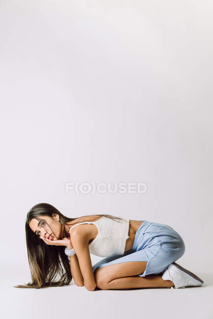 Visão lateral da jovem mulher hispânica com cabelos longos tocando o rosto enquanto se inclina para a frente e olhando para o chão — Fotografia de Stock