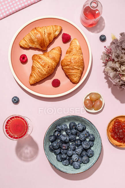 Сверху композиция покрыта свежими выпеченными сладкими круассанами, подаваемыми с ягодами и вареньем, помещенными на розовый стол — стоковое фото