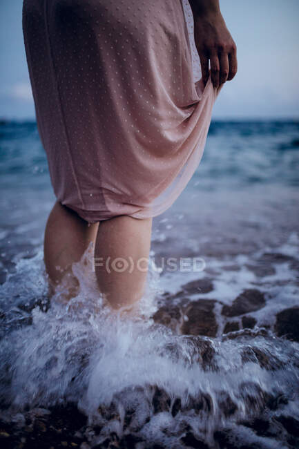 Vista posteriore del raccolto femminile irriconoscibile in abito rosa in piedi in acqua di mare in estate sera — Foto stock
