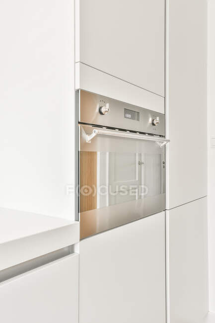Вбудована хромова піч, встановлена в білі шафи на сучасній кухні з мінімалістичним інтер'єром — стокове фото