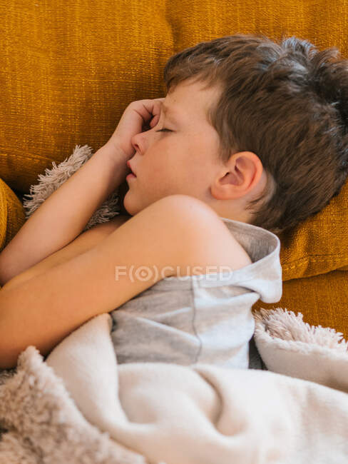 Top view of ill boy having flu lying with closed eyes under blanket on couch and sleeping in living room at home — Stock Photo