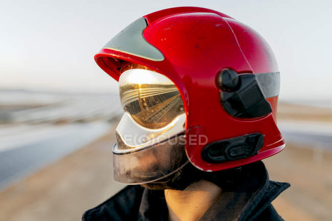 Unrecognizable firefighter wearing protective hardhat and special uniform with yellow reflective patches on background of clear sky in daytime — Stock Photo