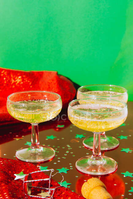 Glass goblets of fizzing champagne placed on table covered with confetti against green background during Christmas party — Stock Photo