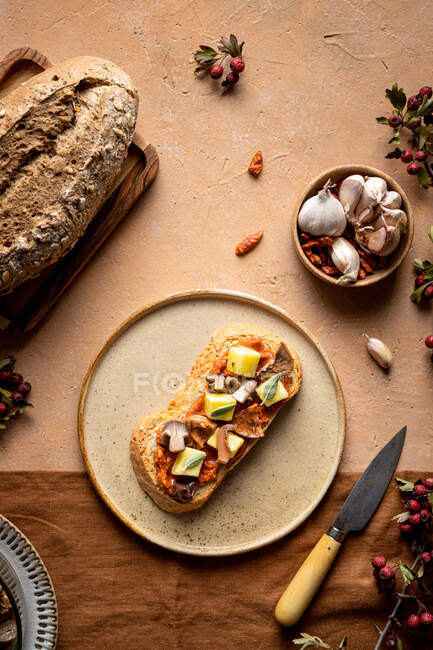 Top view of toast with cheese cubes and slices of mushrooms served on plate near loaf of fresh bread and bowl of garlic in kitchen — Stock Photo