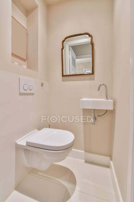 Белый туалет и раковина, установленные на стенах возле зеркала в светлой современной ванной комнате — стоковое фото