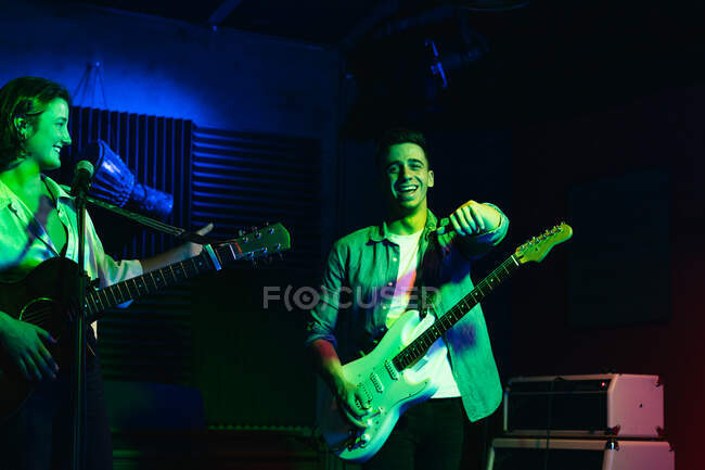 Groupe positif jeune avec microphone et guitares performant en club avec néon vert et lumières bleues — Photo de stock
