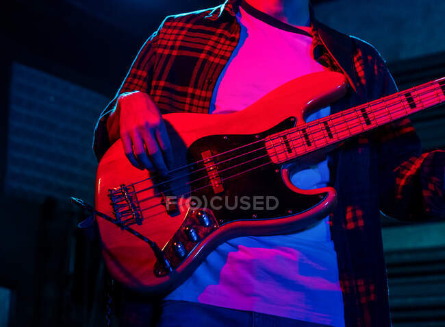 Crop anonymous male guitarist playing electric guitar in club with neon purple and blue lights — Stock Photo