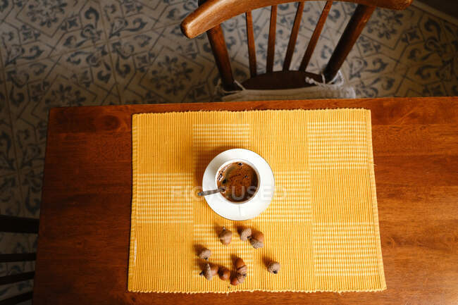 Draufsicht auf Keramiktasse mit frisch gebrühtem Espresso auf Untertasse auf Serviette in der Nähe von Eicheln auf Holztisch — Stockfoto