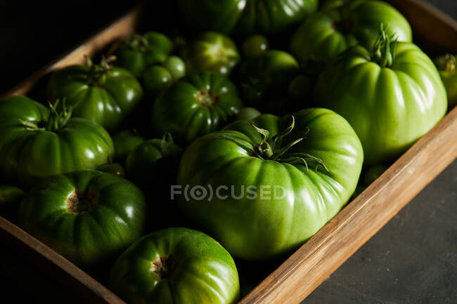 Boîte pleine de tomates vertes non mûres placées sur une table noire à la saison des récoltes — Photo de stock