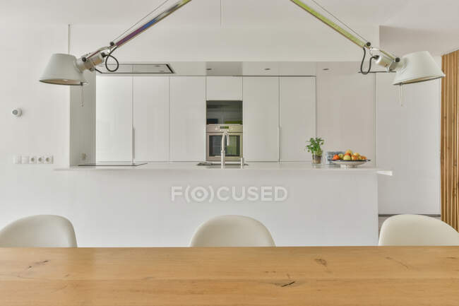 Творчий дизайн інтер'єру кухні та їдальні з дерев'яним столом проти вбудованої печі та мікрохвильової печі в будинку — стокове фото