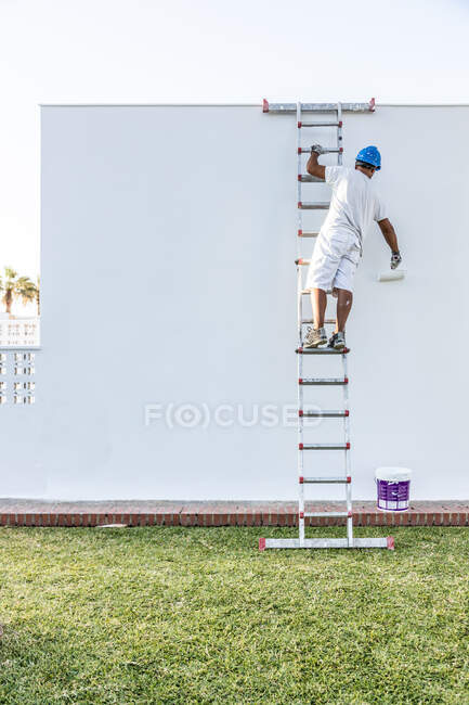 Jeune peintre méconnaissable peignant la façade d'un appartement avec un rouleau de l'escalier — Photo de stock