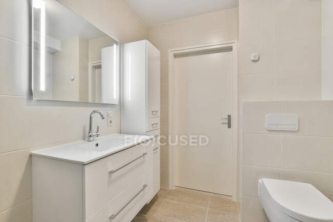 Interior do banheiro contemporâneo com lavatório e armário sob espelho contra vaso sanitário em casa com lâmpadas brilhantes — Fotografia de Stock