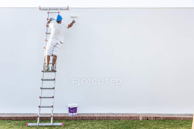 Unrecognizable young painter painting the facade of an apartment with a roller from the staircase — Stock Photo