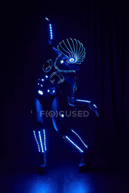Gesichtslose Person im zeitgenössischen leuchtenden Raumanzug eines Cyborg mit Neon-Beleuchtung und Helm auf schwarzem Hintergrund im dunklen Studio — Stockfoto