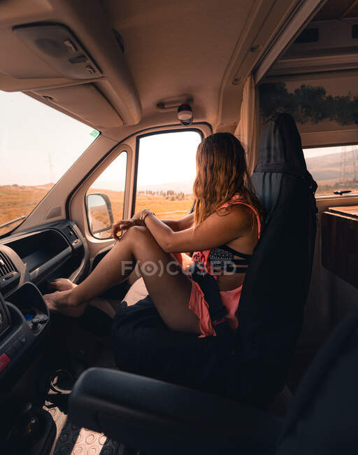 Vista lateral de una viajera irreconocible sentada en el asiento del pasajero en un autocaravana ambulante estacionada en carretera en las tierras altas de España - foto de stock