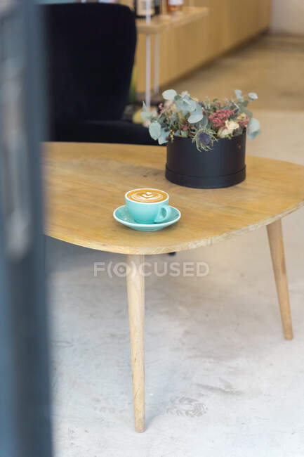 Mug of hot coffee with creative latte art served on plate with teaspoon on wooden table in modern light coffee house — Stock Photo