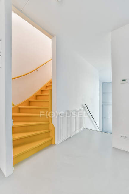 Ondulada escalera vacía contra pasillo con valla y paredes blancas en casa de luz contemporánea - foto de stock