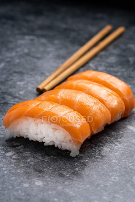 Ensemble de sushis japonais traditionnels similaires avec du riz blanc et du saumon frais servis sur une table en marbre près de baguettes en bois dans la pièce lumineuse — Photo de stock
