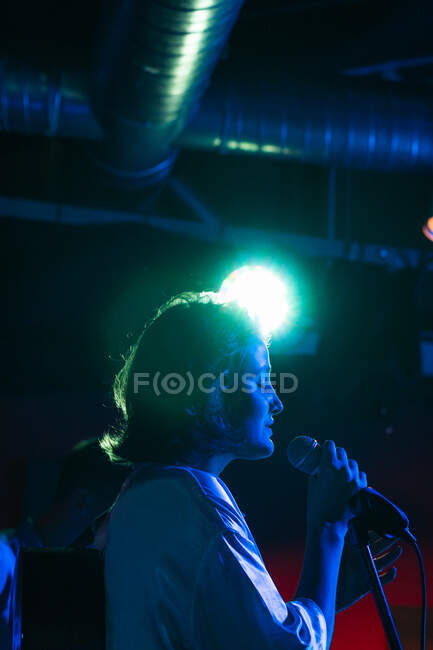Confident lady with guitar singing in mic while performing song in bright club with neon light — Stock Photo