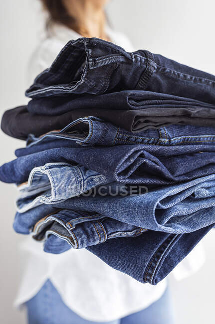 Crop anonymous female in white shirt with stack of blue jeans in hands — Stock Photo