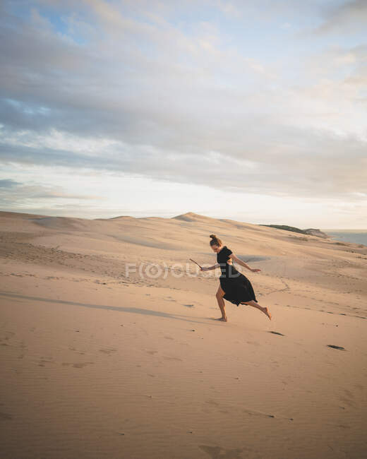 Vista trasera de cuerpo completo de una hembra descalza irreconocible en vestido paseando al atardecer en una duna de arena en el desierto - foto de stock