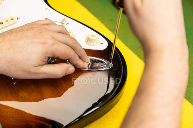 Crop mestre luthier masculino anônimo usando chave de fenda ao fixar guitarra elétrica na mesa em oficina de luz — Fotografia de Stock