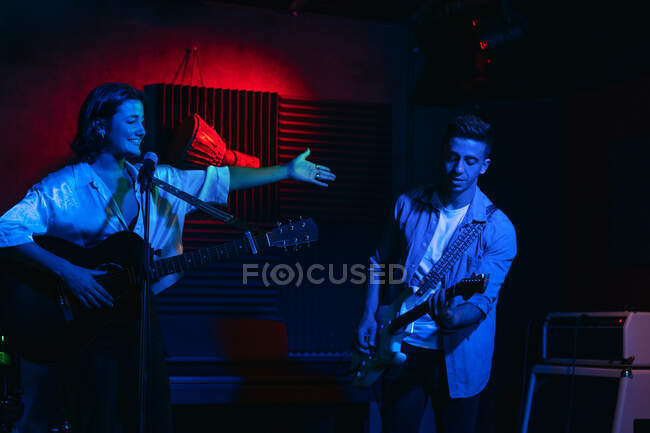 Чоловік грає на гітарі, а жінка співає і виконує пісню в клубі з неоновими вогнями — стокове фото