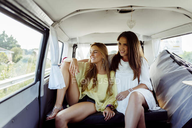 Dos chicas caucásicas lindas sentadas dentro de una furgoneta vestida con ropa de verano mirando por la ventana - foto de stock