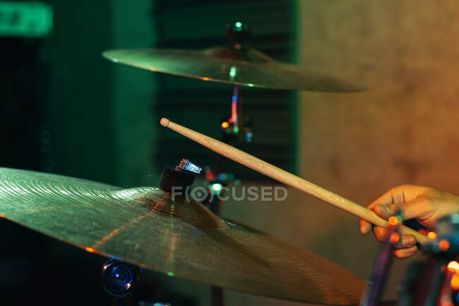 Обрезанный неузнаваемый концентрированный мужчина-музыкант, играющий на барабанах в клубе с зеленой и синей неоновой подсветкой — стоковое фото