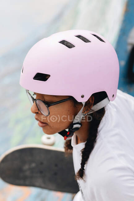 Young African American female in eyeglasses wearing light lilac protective helmet skating in park — Stock Photo