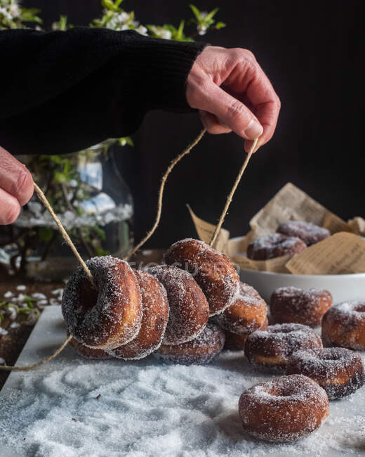 Врожай невизначена жінка тримає смачні позичені пончики в цукровому порошку на нитці за столом — стокове фото