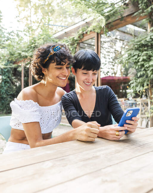 Contenido amigable hembras multirraciales navegando en el teléfono móvil mientras disfrutan de fin de semana juntos en el parque de verano - foto de stock