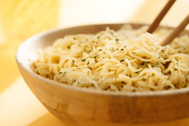 Close-up of bowl of delicious noodles with seasoning placed on yellow background with wooden chopsticks in light room — Stock Photo