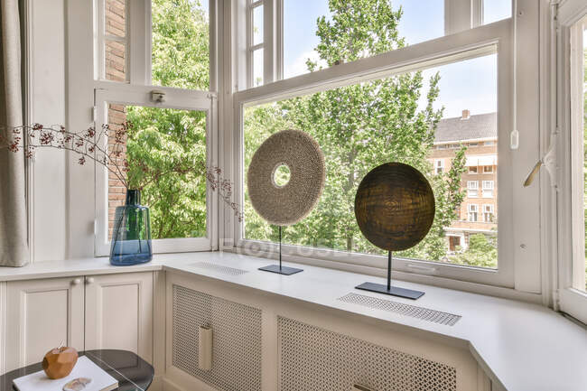 Decoraciones redondas y ramitas en jarrón de vidrio colocado en el alféizar de la ventana en la sala de luz del apartamento moderno - foto de stock