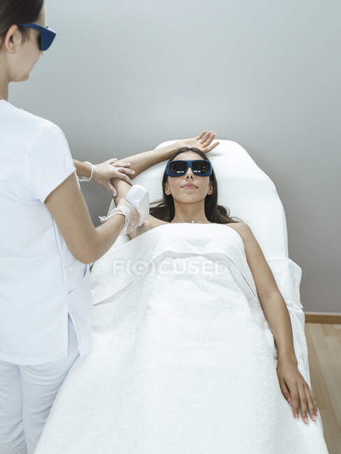 Giovane maestro in maschera che fa la procedura di depilazione laser con attrezzature professionali in mano nel salone leggero — Foto stock