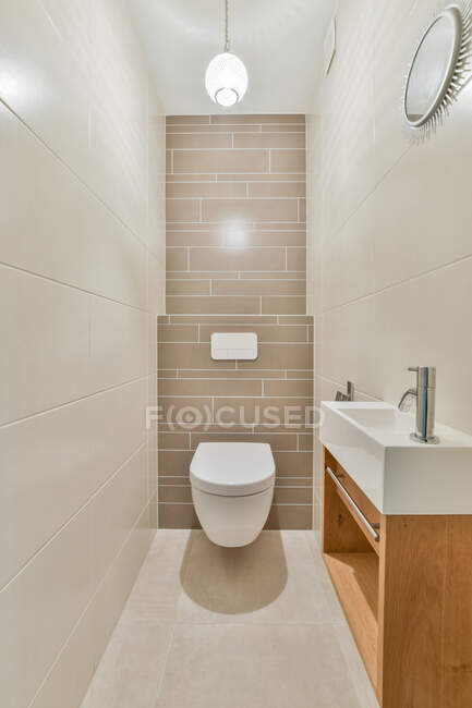Diseño creativo de baño con lavabo contra inodoro y pared de azulejos en casa con luz brillante - foto de stock