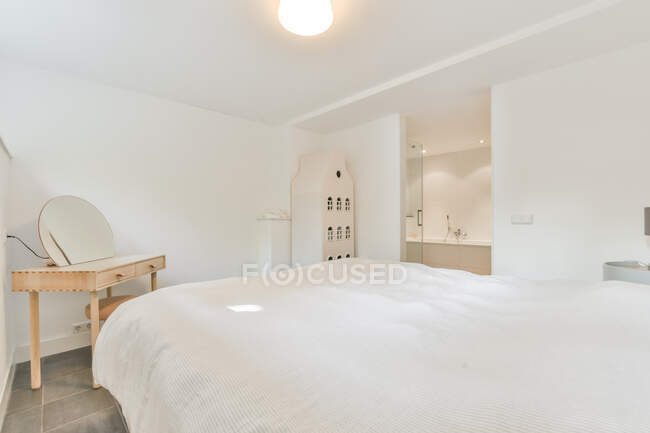 Interior minimalista de dormitorio suite luminosa con cama cómoda y tocador con silla - foto de stock