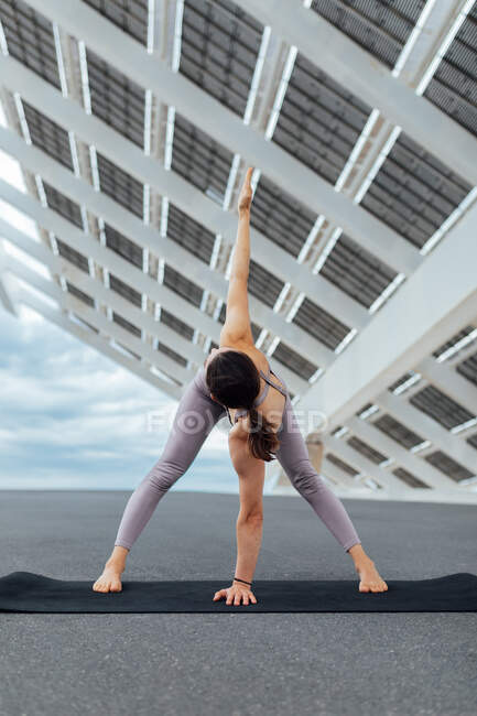 Ganzkörper einer gesichtslosen, aktiven Barfüßerin in Trikonasana-Haltung in Sportbekleidung, die Yoga auf der Straße in der Nähe von Solarzellen in der Stadt praktiziert — Stockfoto