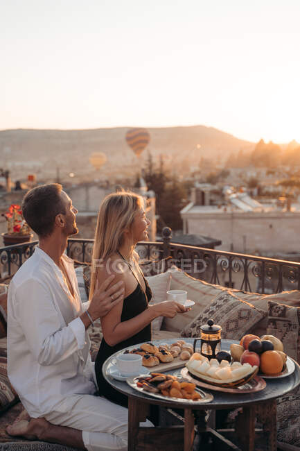 Side view of loving male embracing wife while eating dessert and drinking tea together on terrace — Stock Photo