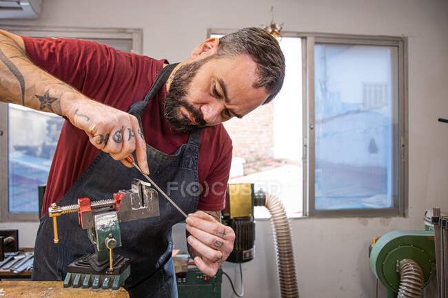Serious male master using screwdriver while working near various machines and windows in light workshop — Stock Photo