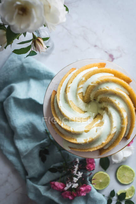 Vista superior del delicioso pastel de esponja de lima servido en un plato blanco cerca de flores y rodajas de lima - foto de stock