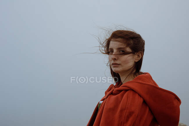 Mulher sonhadora com cabelos longos em roupa estilo vitoriano com capa em pé contra o céu nublado na natureza — Fotografia de Stock