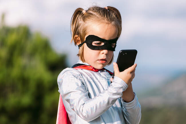 Самозабезпечена дівчина в костюмі супергеройської маски з мисом, що переглядає мобільний телефон — стокове фото