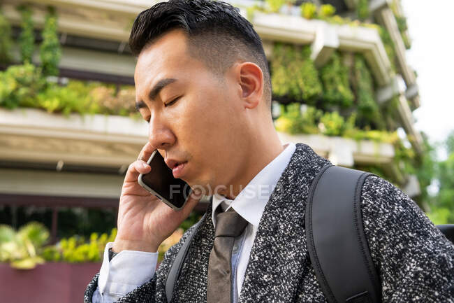 Young ethnic male entrepreneur with tie looking forward while speaking on cellphone in town — Stock Photo