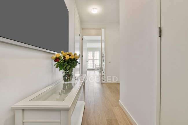 Холл с закрытой белой дверью и стеклянной вазой с букетом цветов в светлых современных апартаментах — стоковое фото