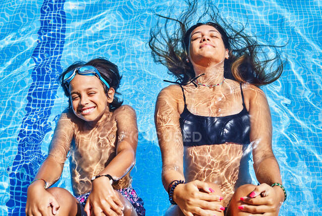 Desde arriba de feliz joven mujer y niño nadando en la piscina con agua cristalina en verano - foto de stock