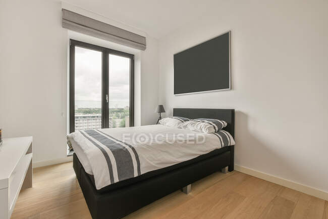 Comodo letto con lenzuola a parete con comodino e TV in elegante camera da letto luminosa con armadio in appartamento — Foto stock